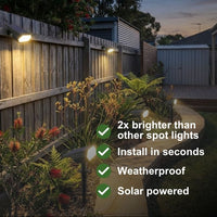 Solar-powered outdoor spot lights mounted on a wooden backyard fence, illuminating plants and a pathway at dusk. White text on the right lists features: '2x brighter than other spot lights', 'Install in seconds', 'Weatherproof', and 'Solar powered'.